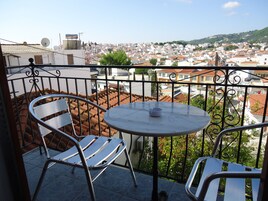 Un balcón con una mesa redonda y dos sillas, con vista a un paisaje urbano de tejados de terracota.
