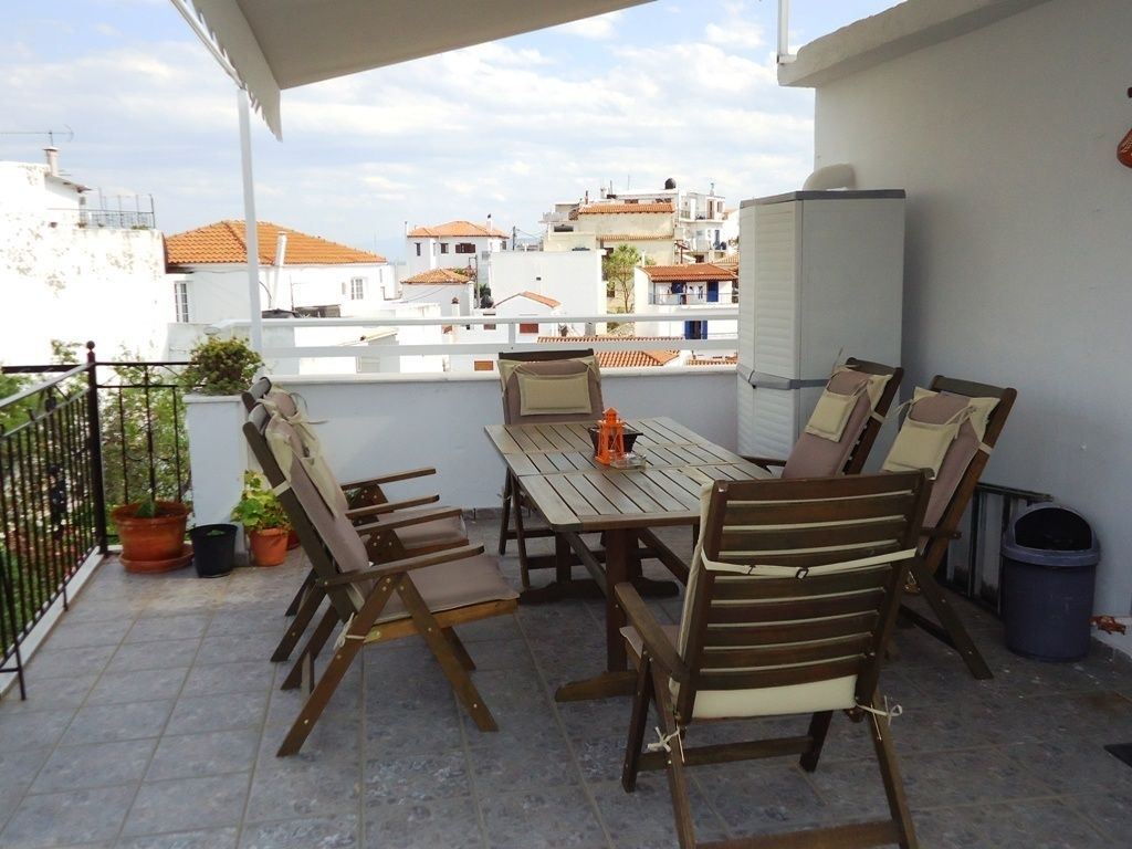 A balcony with a wooden table and chairs, potted plants, and a view of buildings in the background.