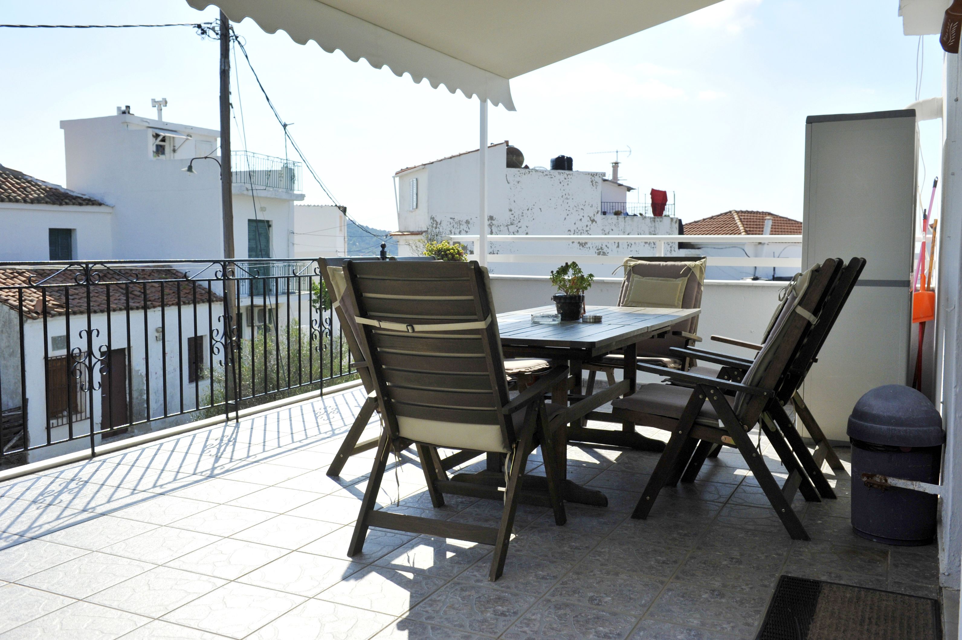 Une terrasse avec une table et des chaises, un pot de fleurs et une poubelle.