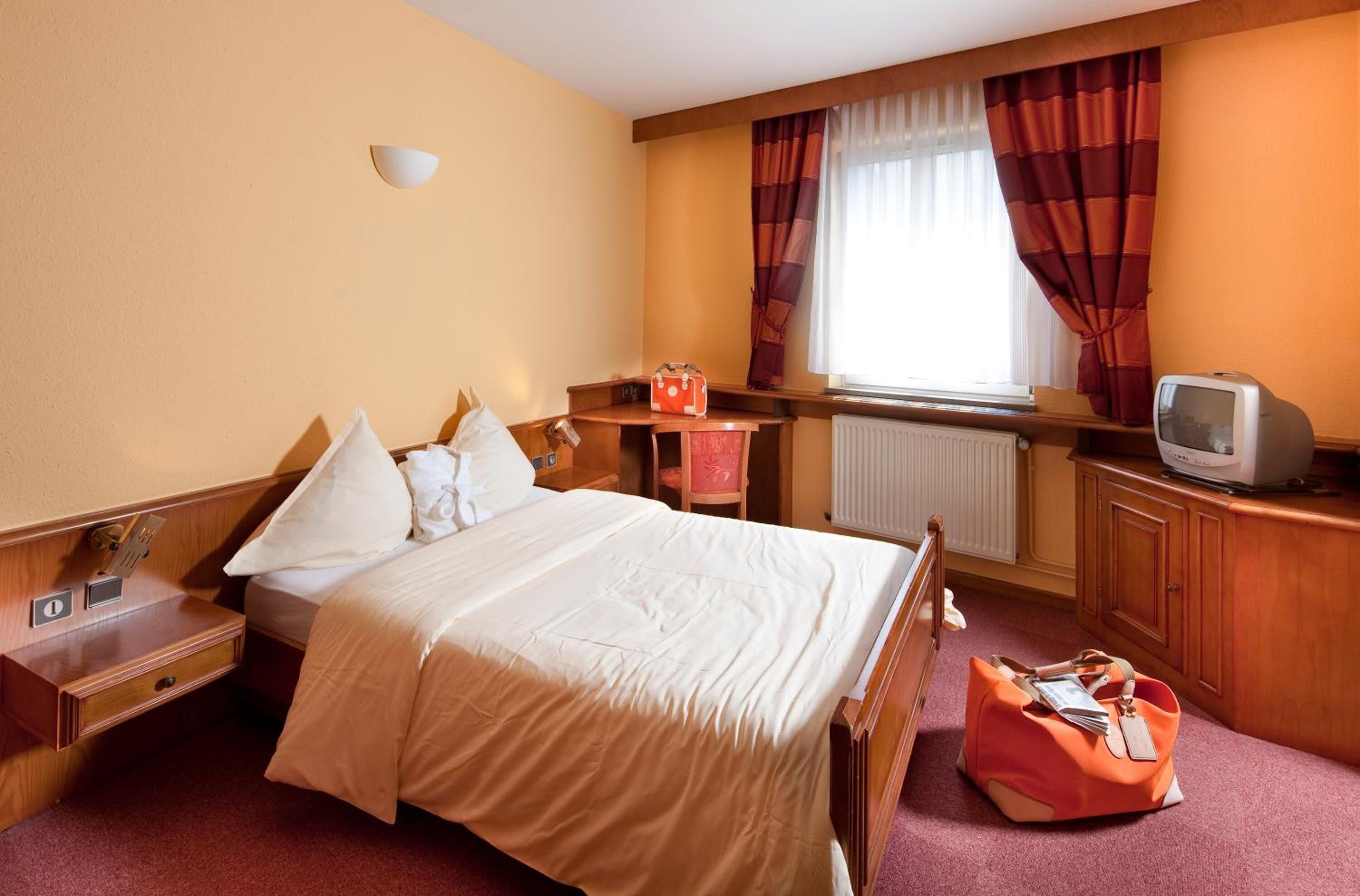 Une chambre d’hôtel avec un lit, un bureau, une chaise, une télévision et une valise.