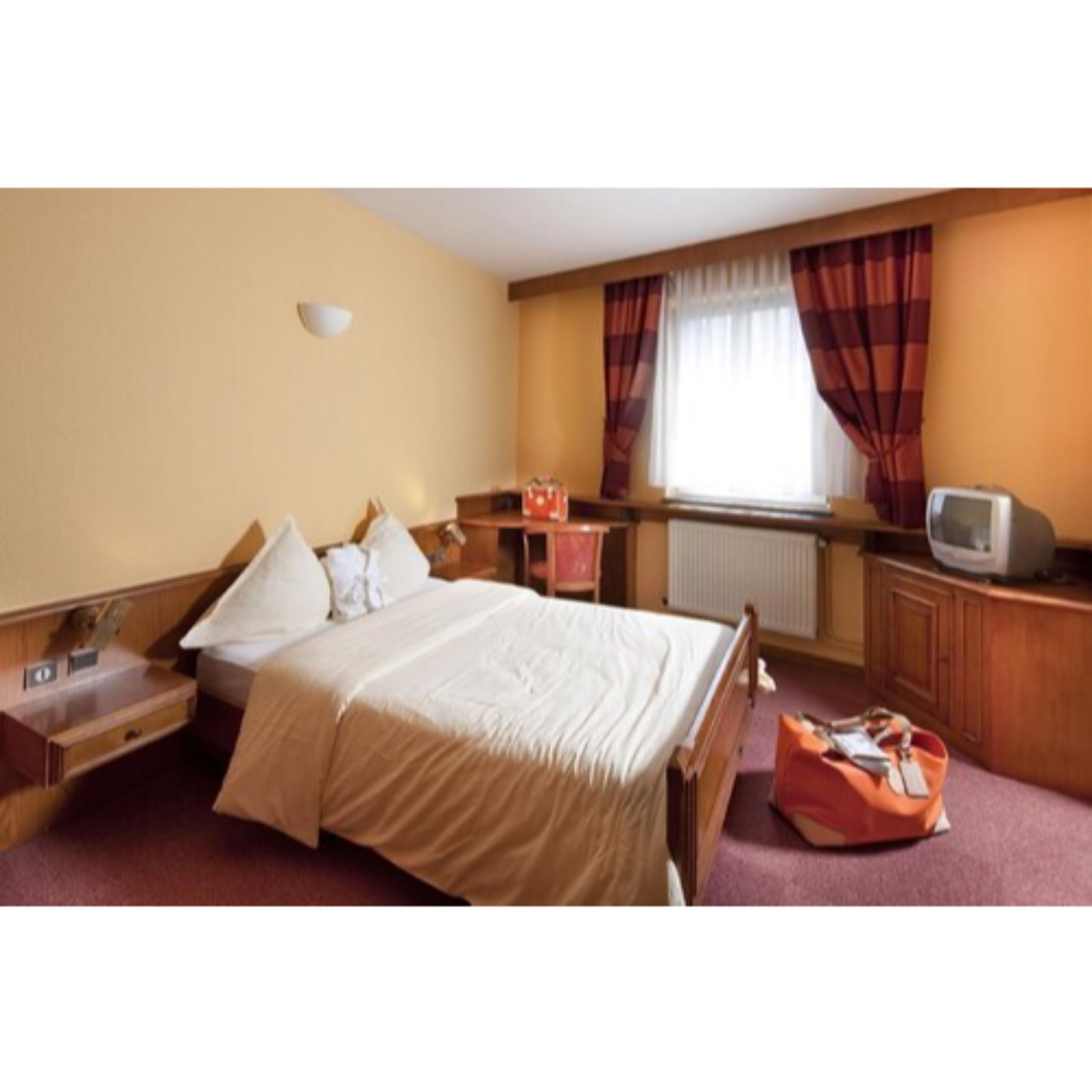Una habitación de hotel con cama, mesita de noche, lámpara, televisor y una maleta.