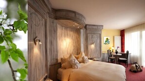 A hotel room with a large bed, a desk with a chair, and a window with curtains. - SPA Hôtel Au Lion D'Or (La Petite-Pierre)