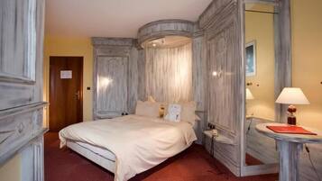 A hotel room with a large bed, a nightstand, a mirror, and a small table with a lamp.