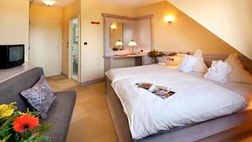 Quarto de hotel com cama, sofá, televisão, espelho e porta do banheiro.