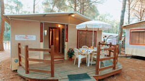 Una pequeña cabaña de una sola habitación con terraza de madera, mesa y sillas, y un letrero que dice "Camp2Relax".