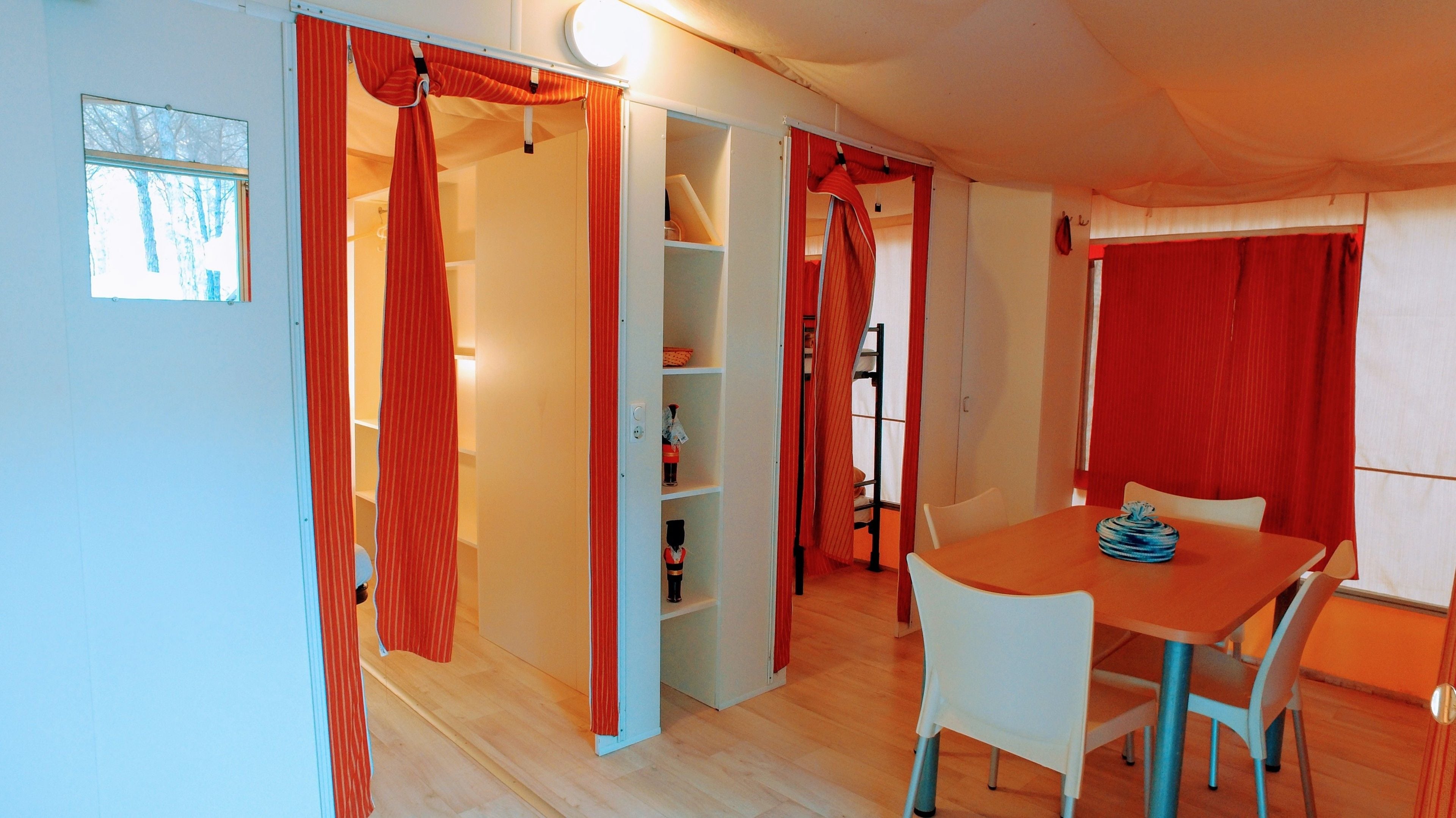 A room with a wooden floor, a dining table with chairs, and red curtains on the doors.