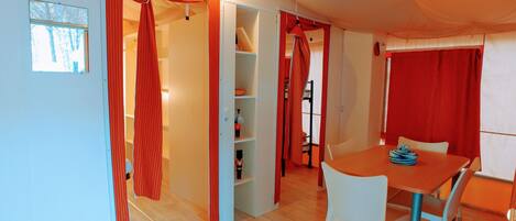 A room with a wooden floor, a dining table with chairs, and red curtains on the doors.