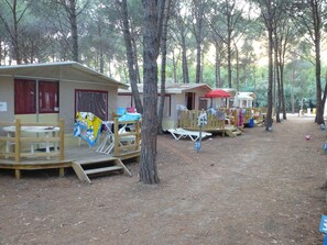 A campsite with wooden cabins, each featuring a small deck and a table. - Spinnaker (Oristano)