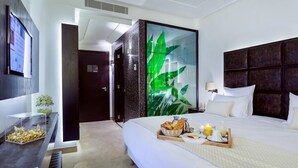 A hotel room with a large bed, a TV, a desk with a vase of flowers, and a green plant wall. - Business Hotel Tunis (Tunis)