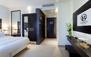 A hotel room with a bed, a nightstand, a mirror, a dark door, a wall-mounted TV, and a sign for Business Hotels. - Business Hotel Tunis (Tunis)