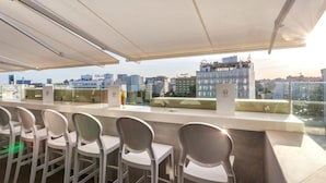 A rooftop bar with white chairs and a glass railing overlooking a cityscape. - Business Hotel Tunis (Tunis)