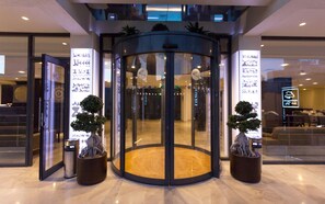 A revolving door with glass panels, two potted plants, and a sign with Arabic script. - Business Hotel Tunis (Tunis)