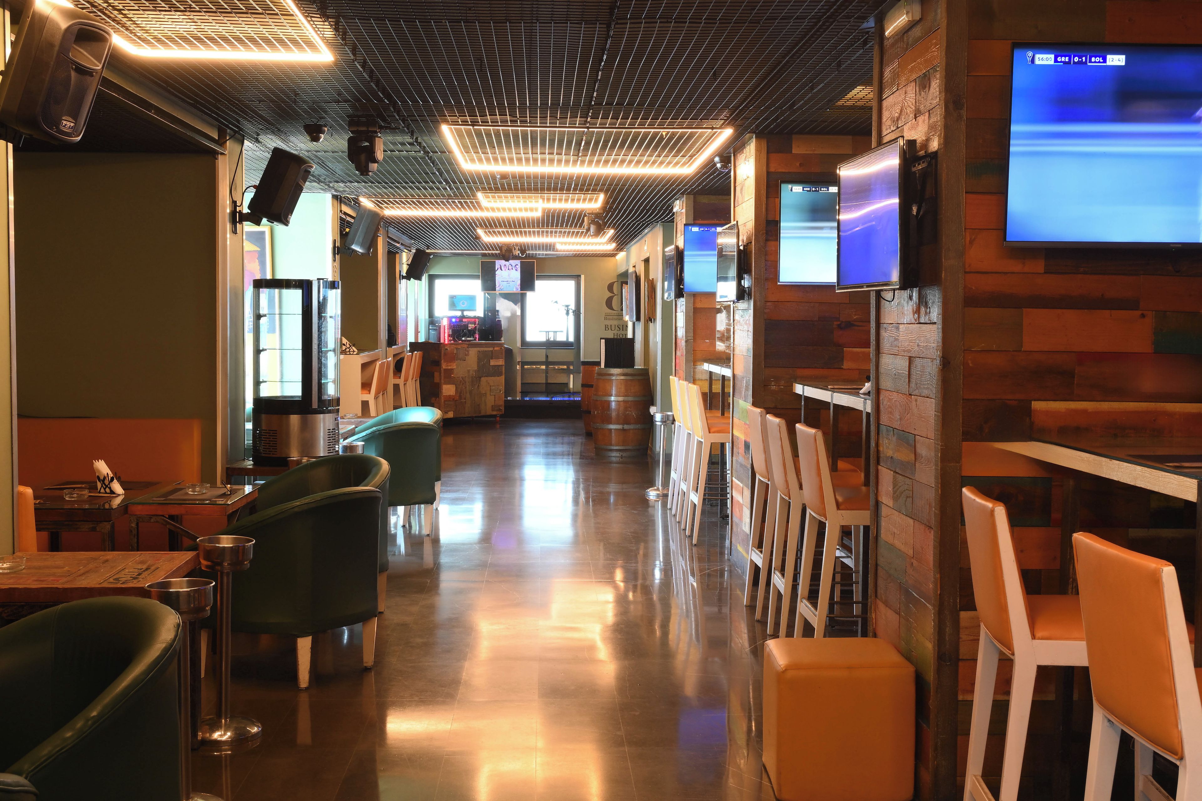 Interior de restaurant amb un taulell llarg, seients en cabines i una pantalla de televisió que mostra un partit esportiu.