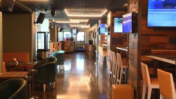 Interior de restaurant amb un taulell llarg, seients en cabines i una pantalla de televisió que mostra un partit esportiu.