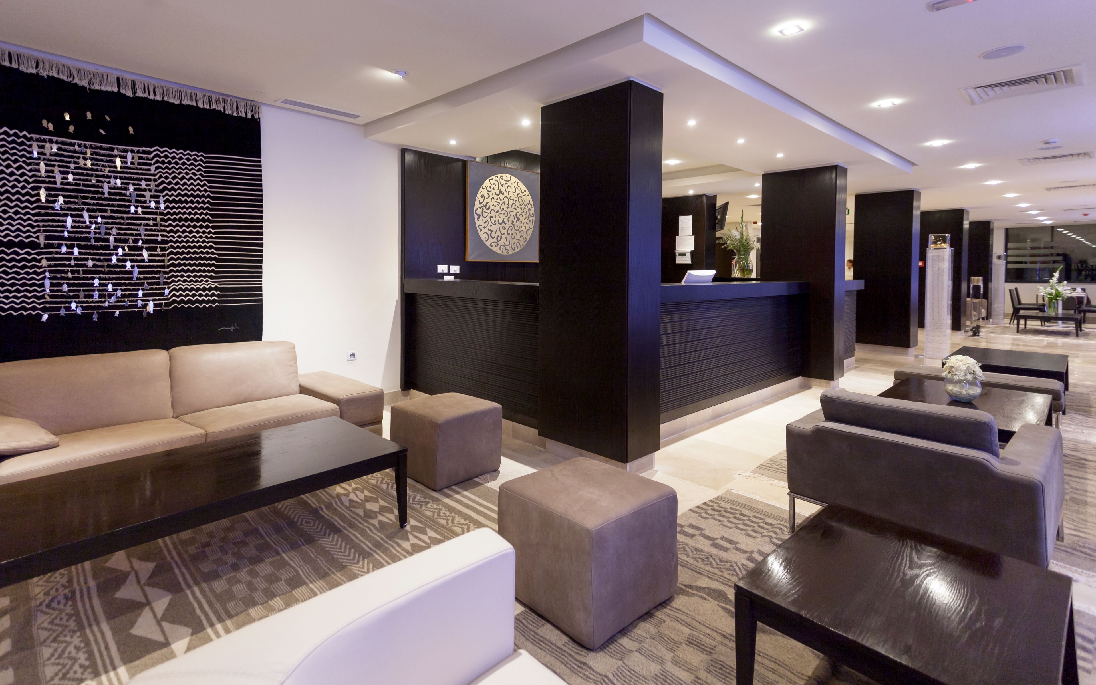 A modern hotel lobby with a reception desk, seating area, and patterned carpet.