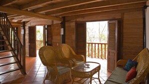 A wooden interior with wicker furniture, a glass table, and a balcony with wooden shutters. - River Ray Estates (Ho Chi Minh City)