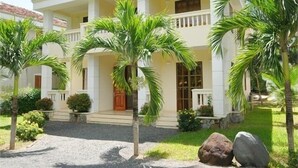 A two-story building with a white facade, a central entrance with a wooden door, and a balcony on the upper floor. - River Ray Estates (Ho Chi Minh City)
