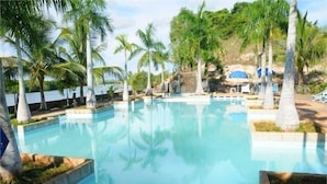 A clear swimming pool surrounded by palm trees and a rocky landscape. - River Ray Estates (Ho Chi Minh City)