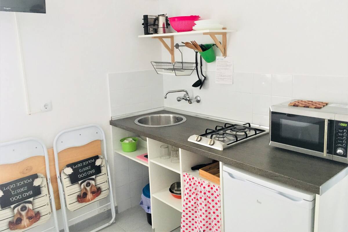 Une petite cuisine équipée comprenant un évier, une cuisinière, un four à micro-ondes et des étagères avec des ustensiles de cuisine.