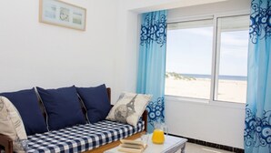 Ein Zimmer mit einem karierten Sofa, einem kleinen Tisch mit Büchern und einem Glas Orangensaft, und einem Fenster mit Blick auf den Strand.