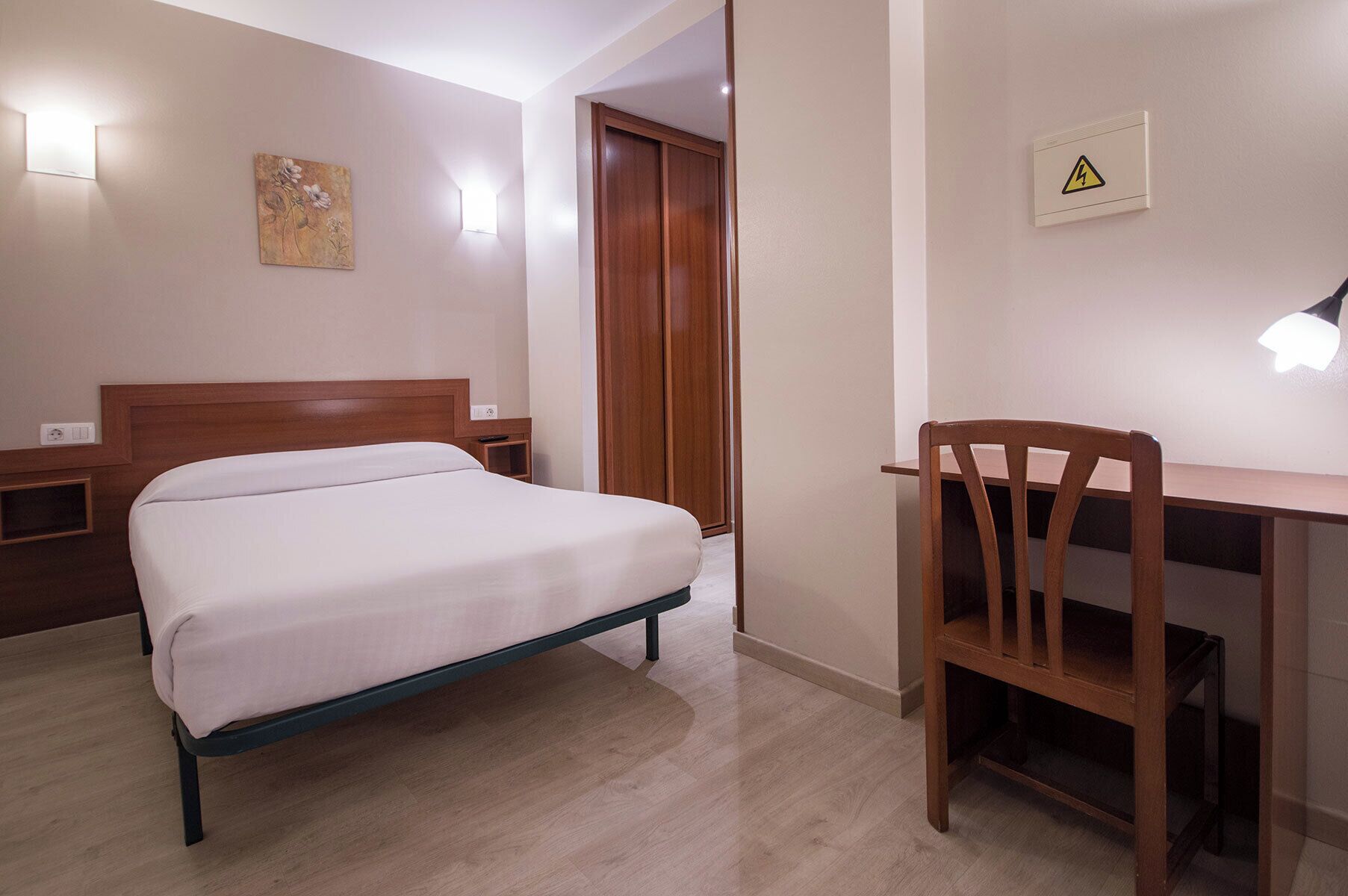 Camera d'albergo con letto, scrivania, sedia, armadio e lampada a muro.