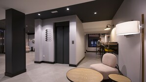 A modern hotel lobby with a reception desk, seating area, and a wall-mounted elevator control panel. - U-Hotel Dario Lugo (Lugo)
