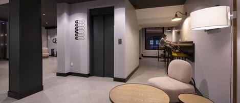 A modern hotel lobby with a reception desk, seating area, and a wall-mounted elevator control panel.