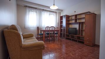 A living room with a sofa, a dining table with chairs, a television, and wooden cabinets.