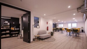 A spacious office with a kitchenette, a grey sofa, and a dining area with yellow chairs. - U-Hotel Dario Lugo (Lugo)