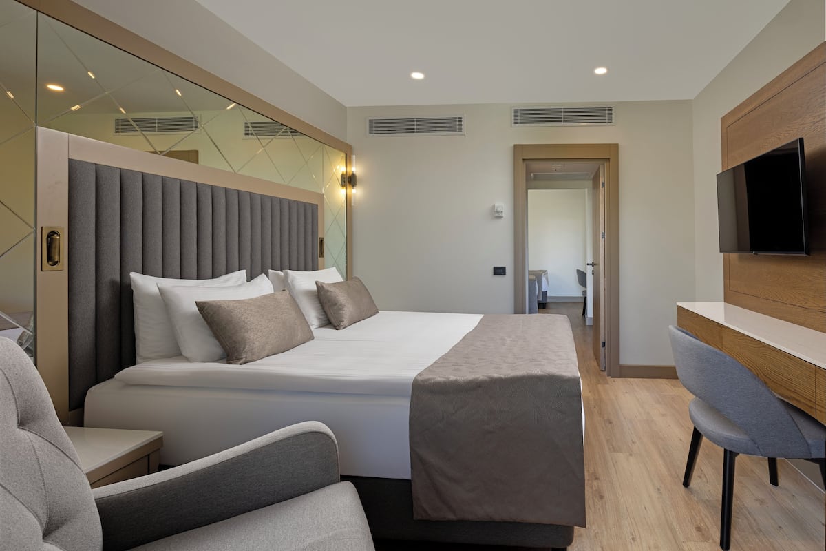 A modern hotel room with a large bed, a desk, a chair, and a TV mounted on the wall.