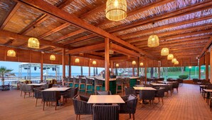 Un restaurant en plein air avec des tables et des chaises en bois, des guirlandes lumineuses et une vue sur l’océan.