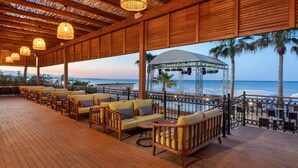 A wooden deck with outdoor seating, a stage, and a view of the beach. - DOBEDAN BEACH RESORT COMFORT (Manavgat)