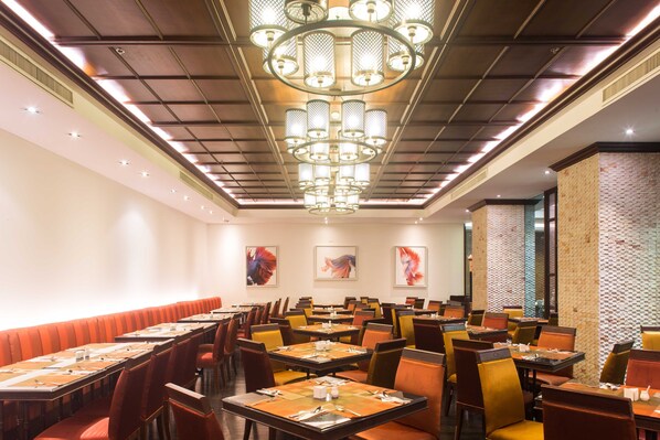 A spacious dining area with multiple tables and chairs, a central chandelier, and artwork on the walls. - Mida Grande Hotel Dhavaravati, Nakhon Pathom (Nakhon Pathom)