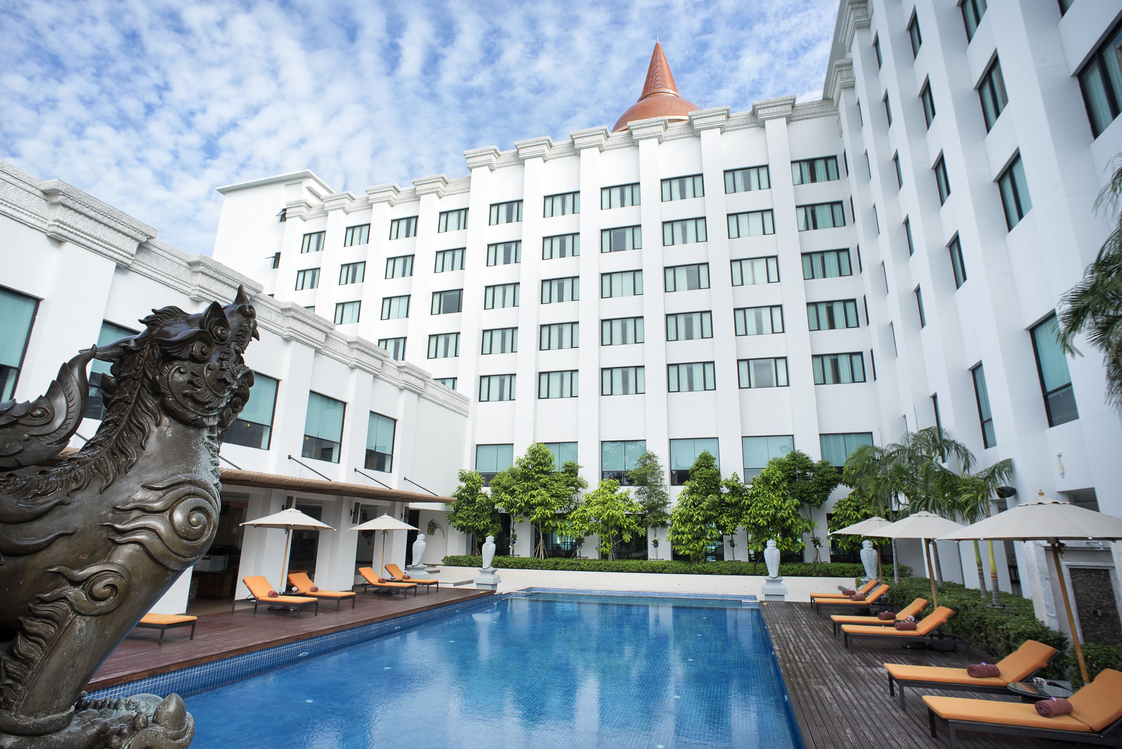 A hotel with a swimming pool, lounge chairs, and a decorative lion statue.