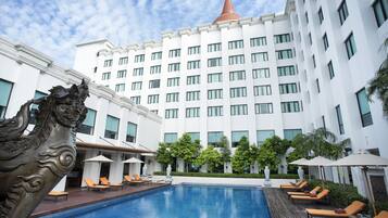 A hotel with a swimming pool, lounge chairs, and a decorative lion statue.