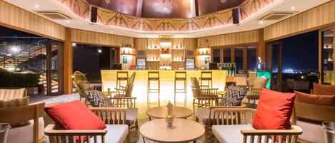 Een ruime lounge met houten meubels, een bar in het midden en grote ramen met uitzicht over de stad.