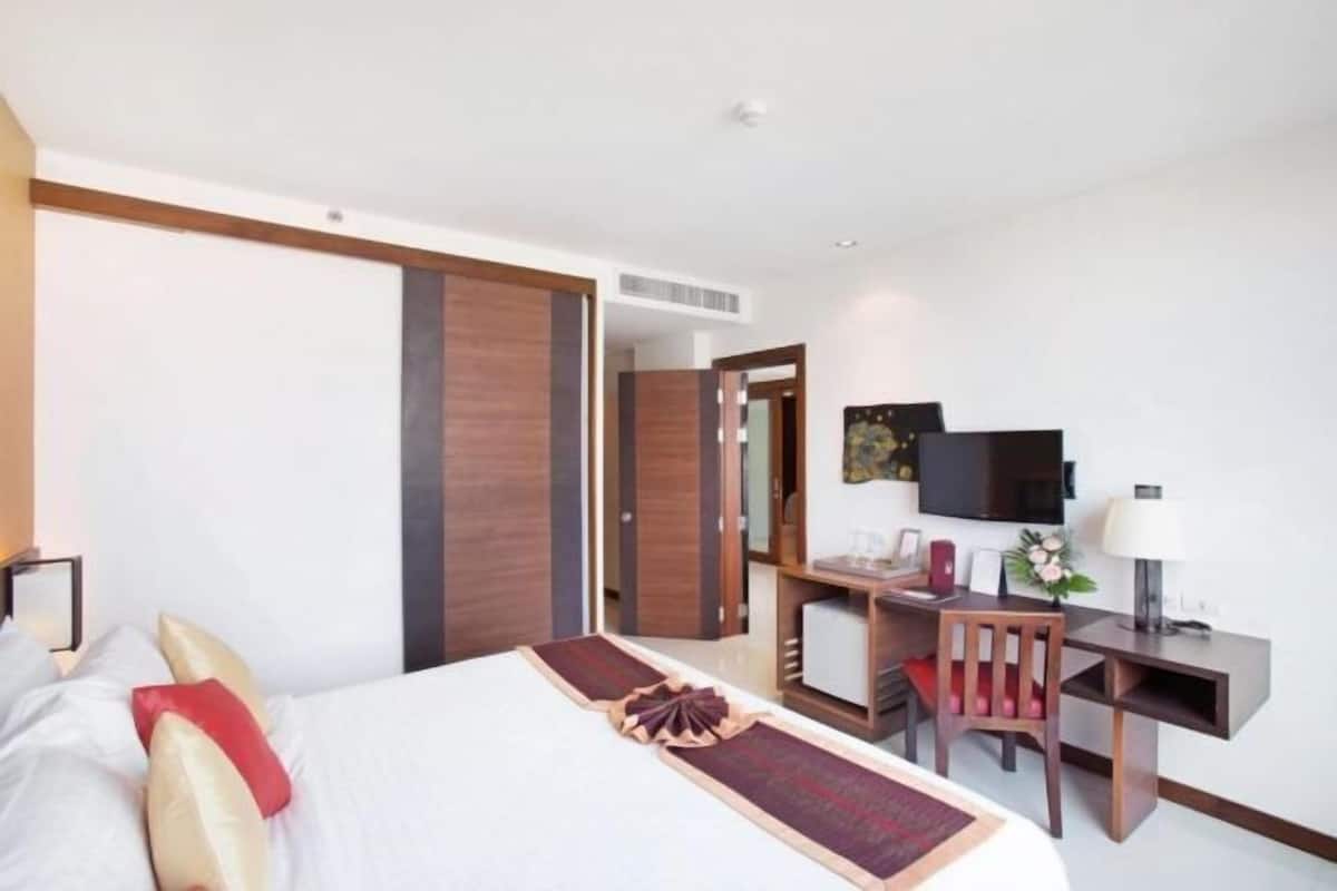 A hotel room with a bed, desk, chair, television, and a door leading to another room.