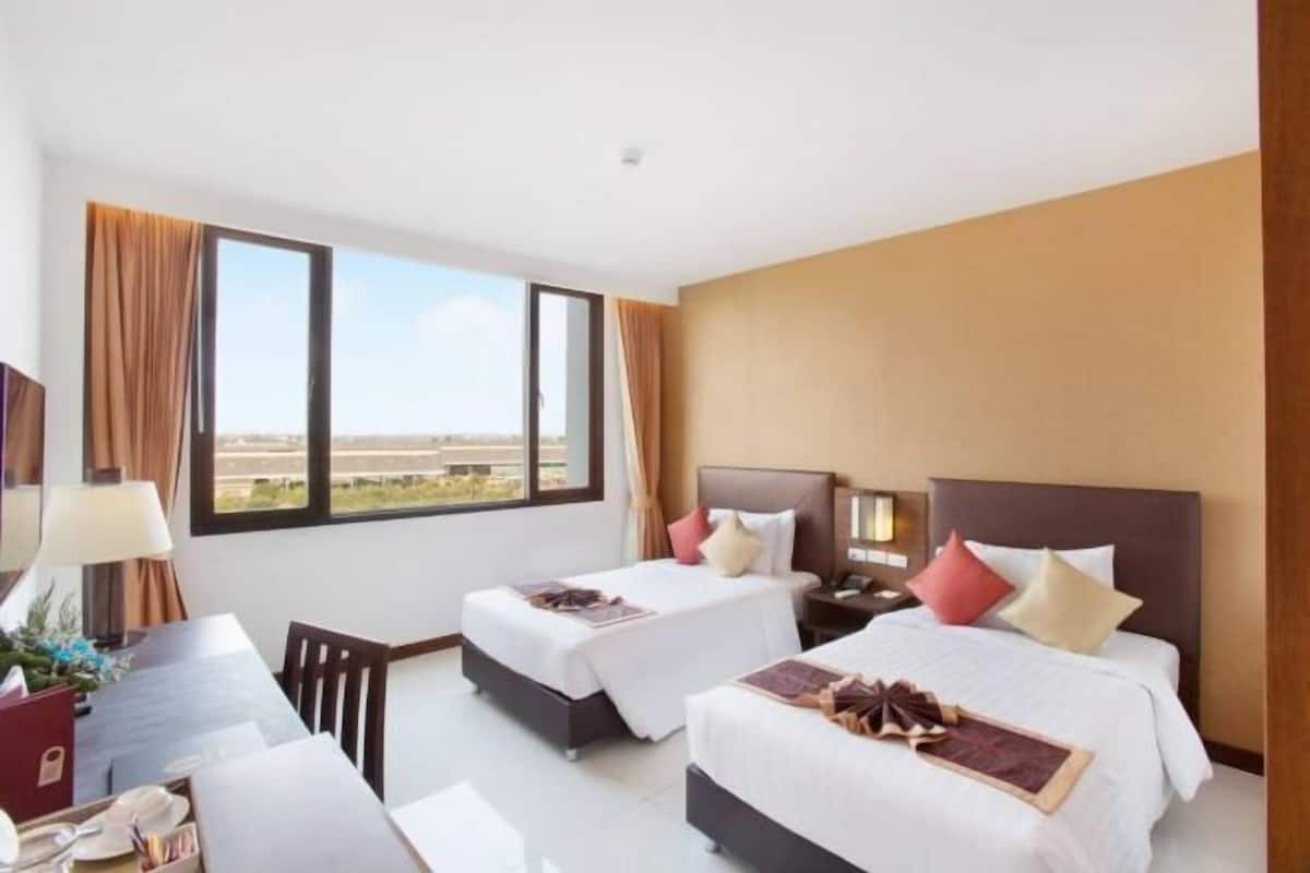 A hotel room with two beds, a desk, and a view of the cityscape.