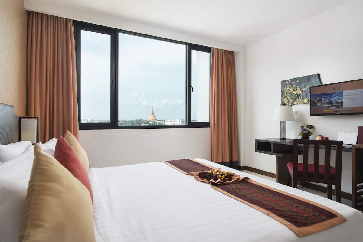 A hotel room with a large bed, a desk, a chair, and a TV.