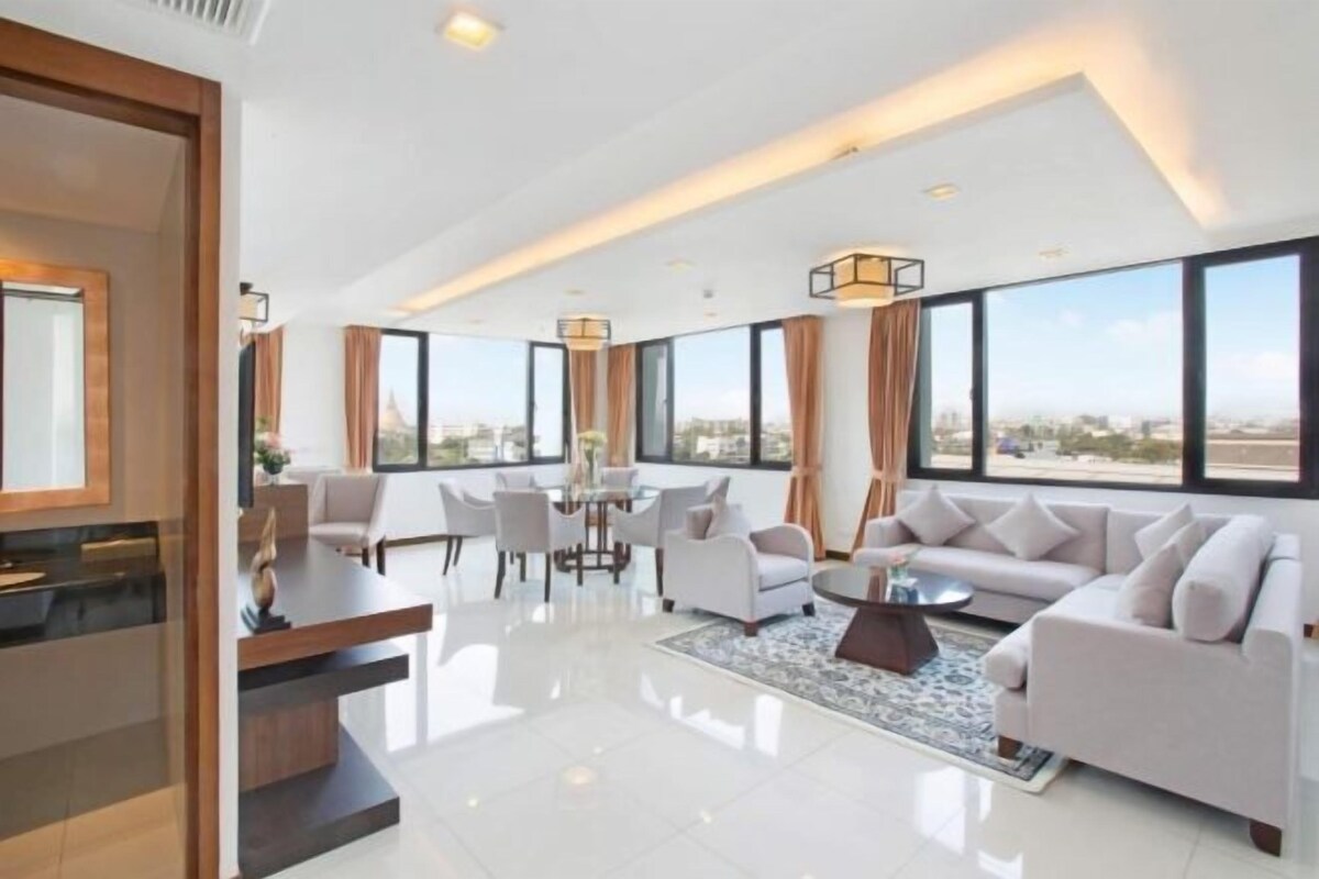 A modern hotel room with a dining area, large windows, and a view of the city.