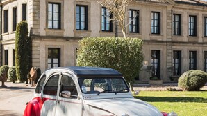 A vintage red and white Citroën 2CV car parked in front of a large, classical building with a tiled roof and multiple windows. - Domaine d'Auriac (Carcassonne)