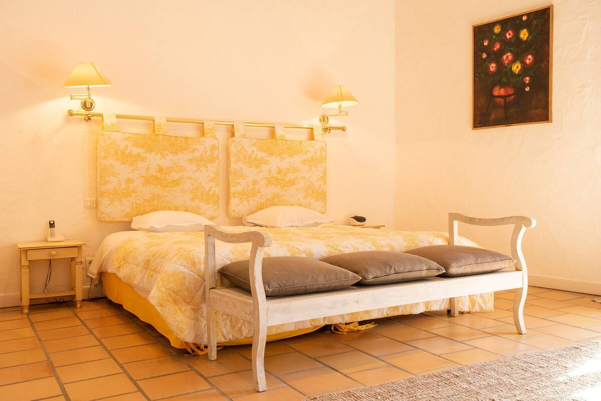 A bed with a headboard, bedside lamps, and a painting on the wall.