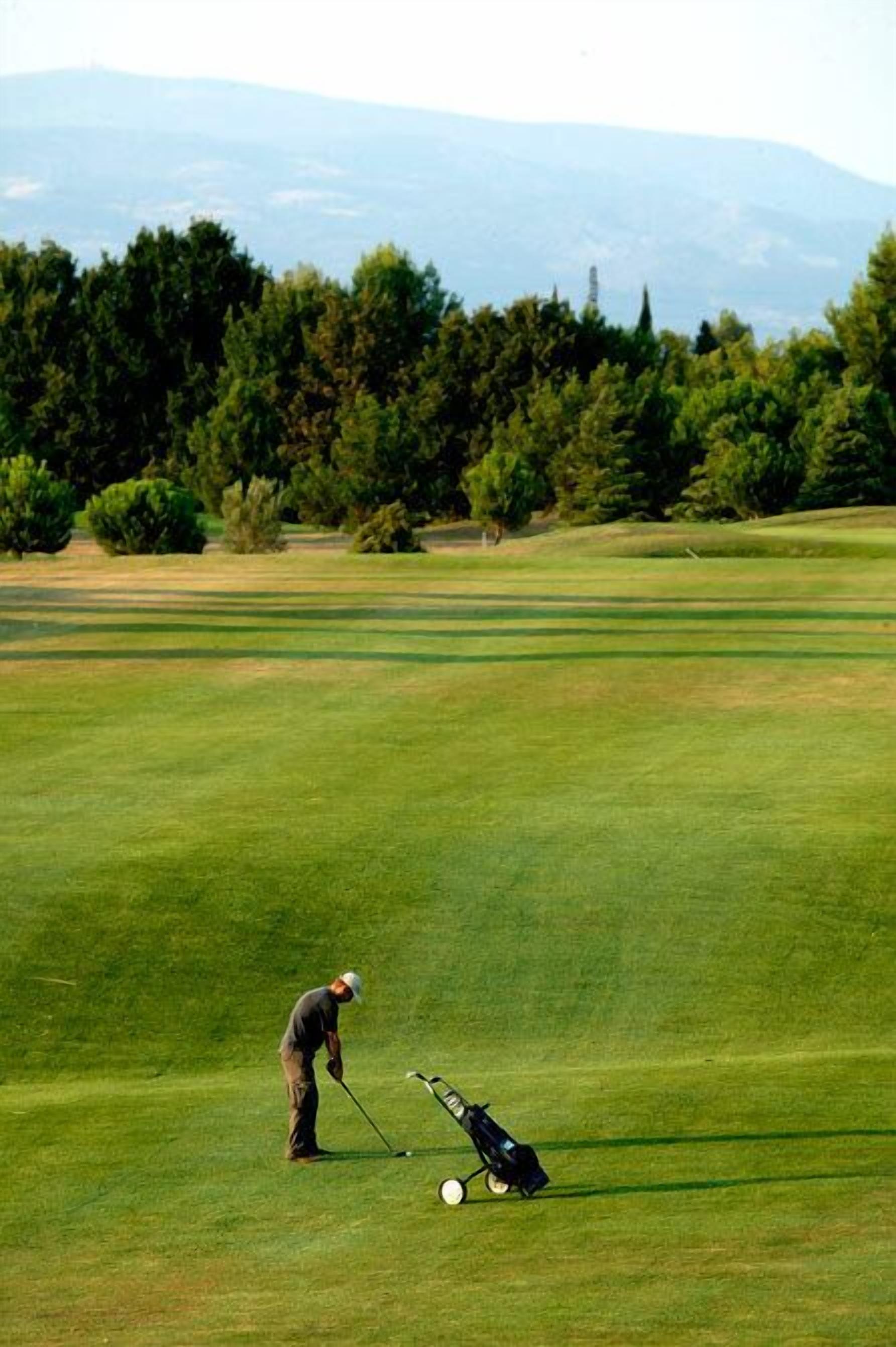 Un terrain de golf où l’on voit un golfeur se préparant à effectuer un putt, un sac de golf et une balle de golf sur le green.
