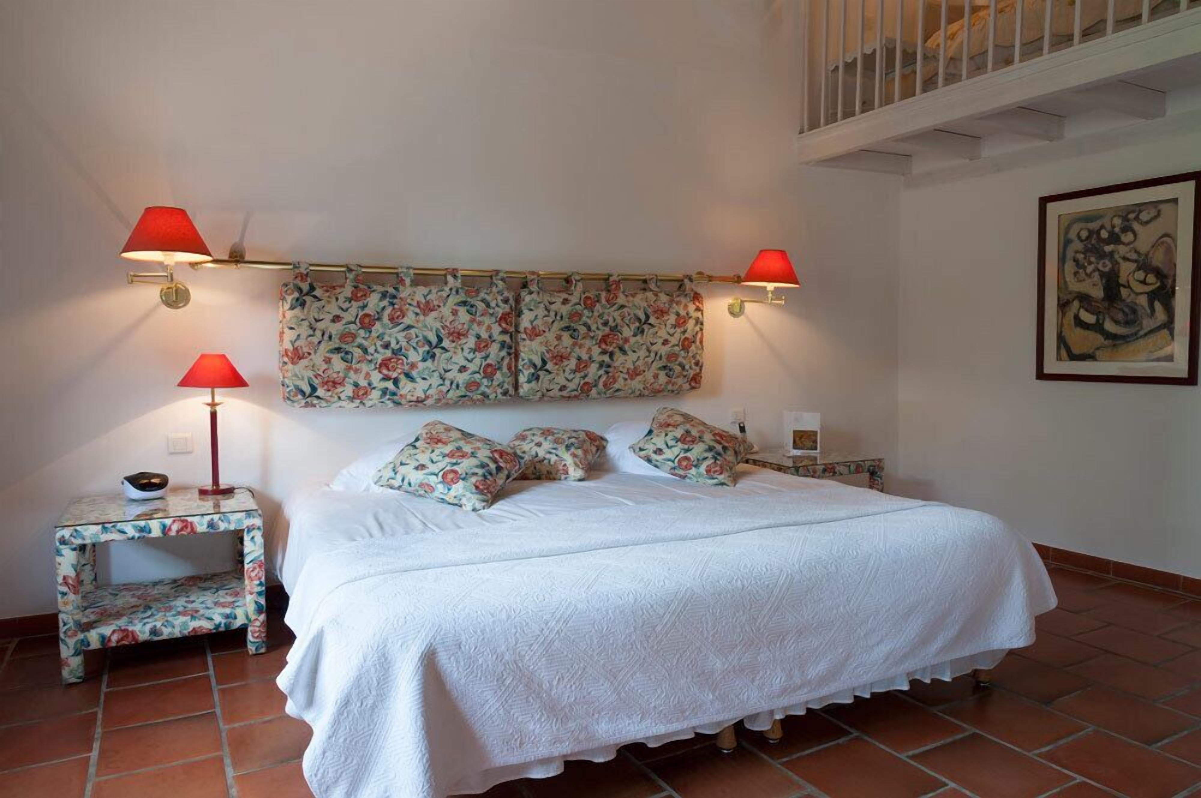 Une chambre à coucher comprenant un lit, deux tables de chevet, une commode, une tête de lit ornée de motifs floraux et deux lampes fixées au mur.
