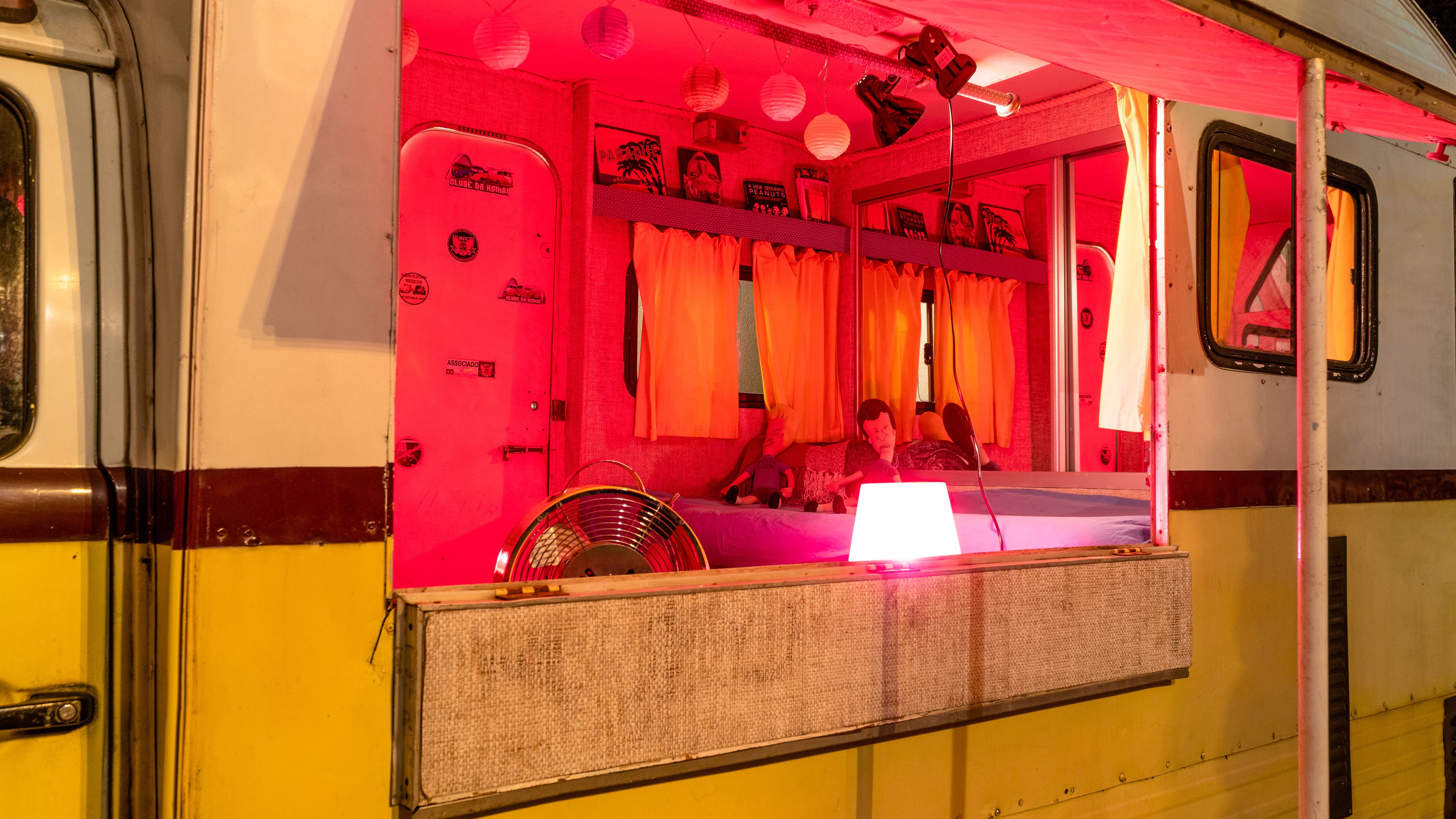 Un compartiment de train avec un intérieur rose, un ventilateur et une fenêtre avec des rideaux.