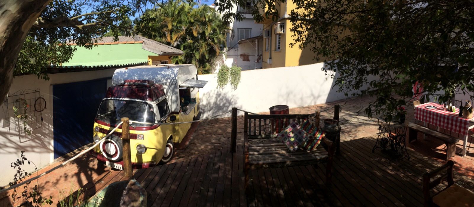 A wooden deck with a table and chairs, a yellow car, and a building in the background.