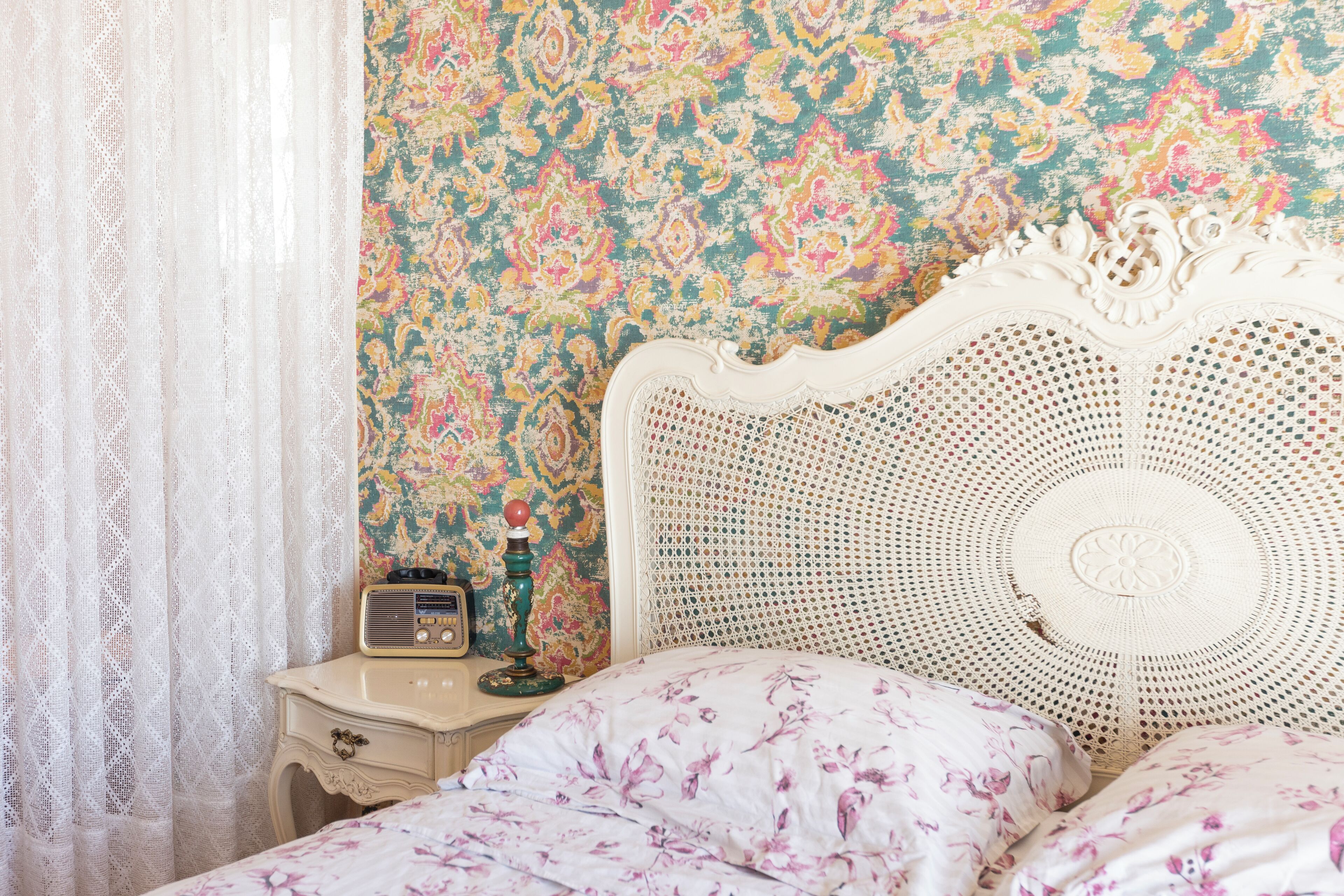 Un lit avec une literie à motifs floraux, une radio ancienne et une tête de lit décorative.