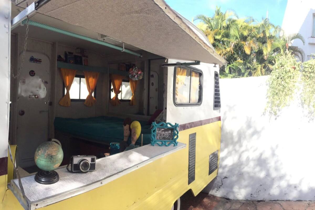A yellow RV with a bed, a globe, and a camera on the dashboard.