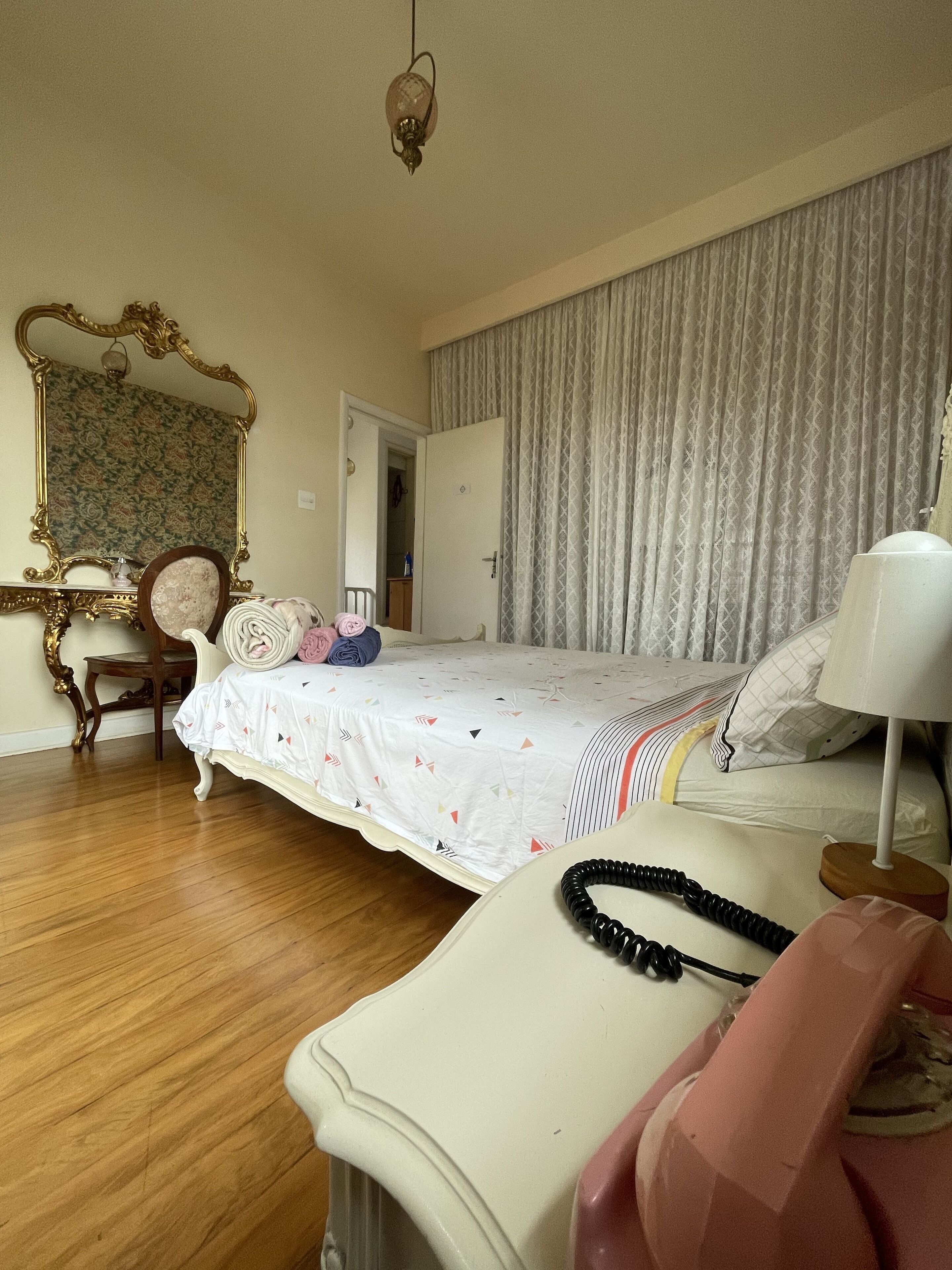 A bedroom with a bed, a vanity with a mirror, a chair, and a bedside table with a lamp.