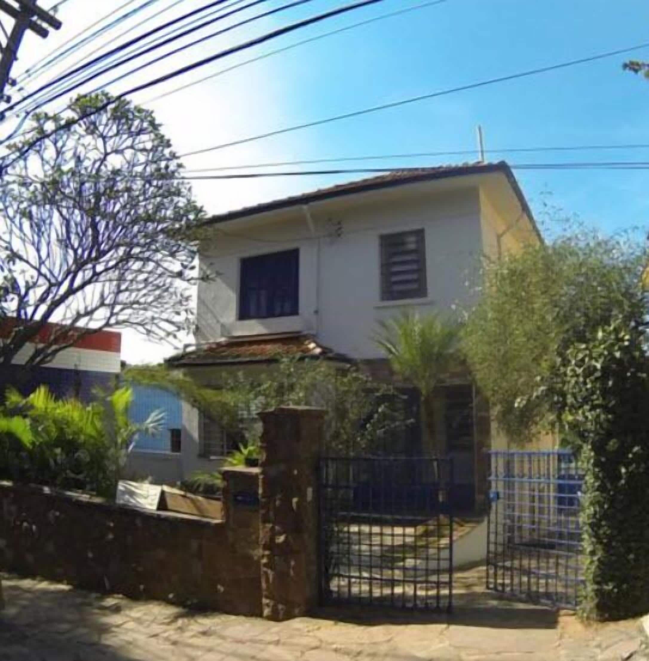 Una casa de dos pisos con fachada blanca, un ventanal en el nivel superior y un muro de ladrillo al frente.